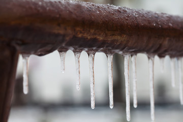 Icicles hanging from a brown pipe. Frozen water and metal surface, winter time concept. selective...