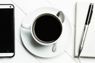 Taza de café con móvil y agenda sobre fondo blanco de madera vista desde arriba 
