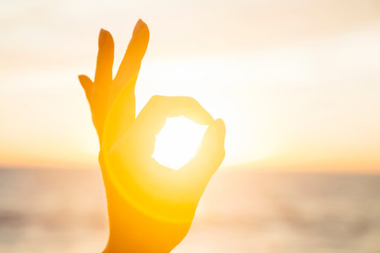 Woman circling the sun with fingers at sunrise