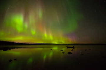 Fototapeta premium Colors of Light - Colorful northern lights bright up the starry night sky and a calm rocky lake.
