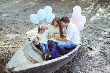 Obraz premium Family portrait. Pregnant woman, man and their daughter sitting in the old boat.