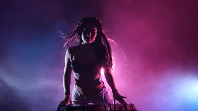 Girl DJ spins a DJ stand, behind her multi-colored lights and smoke. Silhouette