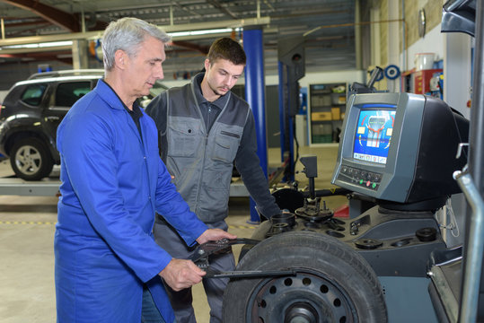 apprentice mechanic and teacher retreading wheel in automotive workshop