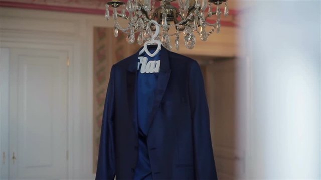 Mans jacket hanging on luster waiting for groom to wear in luxury room interior big day special occasion. Silk fabrics men suit clothing fashion. Henpecked husband male ready for family 