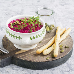 Spring light fresh beet cream soup in portion bowl on a wooden board for feeding with bread sticks. Top view