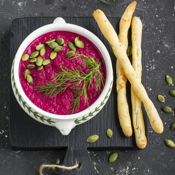 Beet Cream Soup Puree With Pumpkin Seeds, Dill And Bread Sticks On A Dark Background   Blackboard Supply. Top View