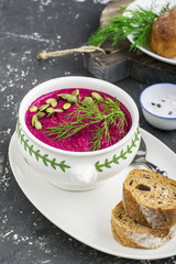 Spring light fresh beet cream soup in portion bowl on a wooden board for feeding with bread. Top