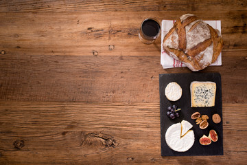 Obraz na płótnie Canvas above overhead view flat lay assortment of various cheese with traditionnal bread fruits glass and bottle of red wine on old wooden table