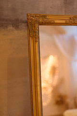 A mirror in a gold frame reflects Christmas interior of bedroom with lights and decor with some blur