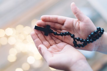 Little boy child praying and holding wooden rosary.