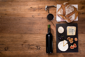 above overhead view flat lay assortment of various cheese with traditionnal bread fruits glass and bottle of red wine on old wooden table