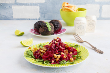 Salad with baked beets, arugula, raisins and walnuts on a green plate on the table in kitchen. Whole beetroots, lime, fresh bread, vintage fork.