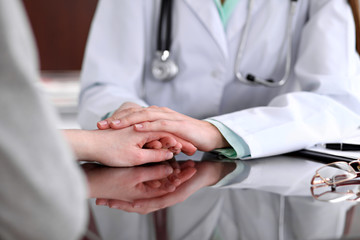 Obraz premium Friendly female doctor hands holding patient hand sitting at the desk for encouragement, empathy, cheering and support while medical examination. Bad news lessening, compassion, trust concept