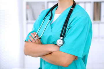 Female surgeon doctor is standing with arms crossed at hospital.  Physician  is ready to examine patient