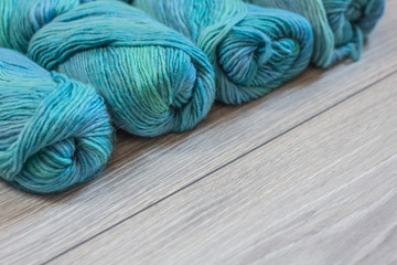Several skeins of blue, green and turquoise yarn lying on a neutral wooden background