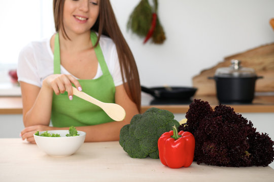 Young woman is cooking healthy meal from vegetables at the kitchen. Close up of housewife with wooden spoon pointing into salad and brocolli. Vegetarian concept.