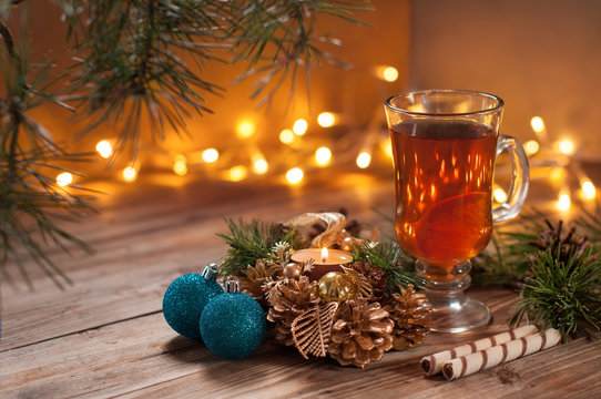Christmas tea in glass Cup . composition with ball, candle, pine branches, pine cones and cookies on background of garlands on wooden table
