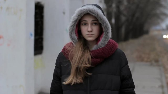 teen runaway: Sad lonely girl hood up standing near old road in cold dark weather, steadicam portrait shot
