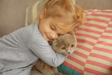 Fototapeta na wymiar Closeup of cute little girl embracing lovely cat on sofa