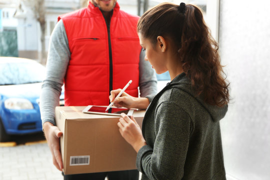 Young woman appending signature after receiving parcel from courier