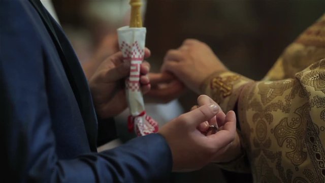 Orthodox priest performing rite of exchanging rings for marrying couple bride and groom at wedding ceremony in church hands fingers close up. Ceremonial clothing golden vestment in orthodox tradition