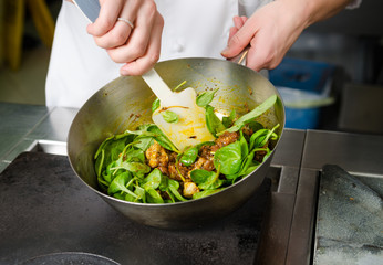 Mixing a curried cauliflower, spinach and potato sauce, in a metal pan.
