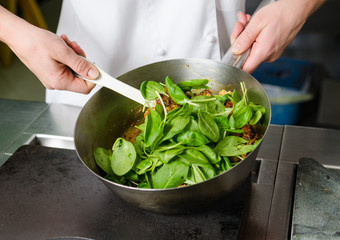 Mixing a curried cauliflower, spinach and potato sauce, in a metal pan.
