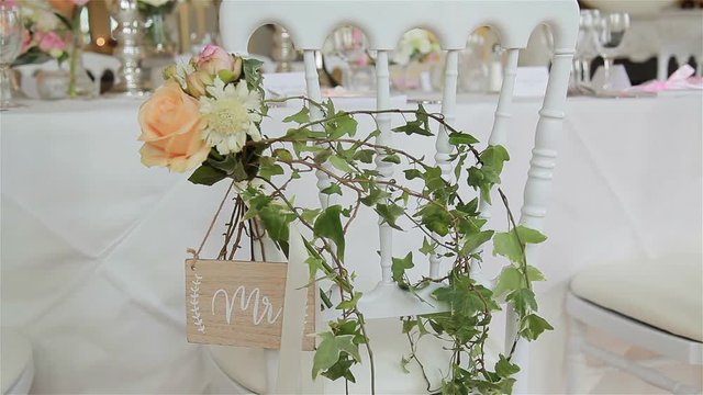 Green wedding decor on chair for reception close up. Flower bouquet and wild ivy twigs used as decoration at white chair arranged in guest seat area. Wedding plan florist work floral elements decision