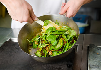 Mixing a curried cauliflower, spinach and potato sauce, in a metal pan.