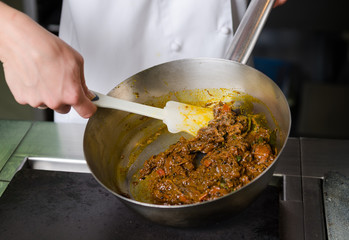 Mixing a curried cauliflower, spinach and potato sauce, in a metal pan.