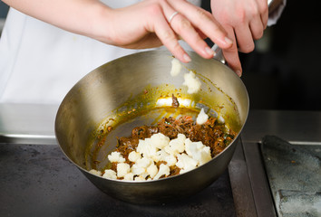 Mixing a curried cauliflower, spinach and potato sauce, in a metal pan.