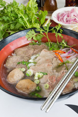 A bowl of traditional vietnamese beef and chicken pho street food, surrounded by fresh herbs. Pho is a vietnamese noodle soup consisting of meat, herbs, chilli, coriander and dumplings.