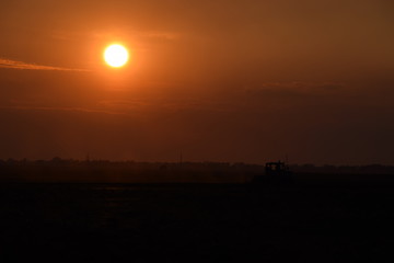Tractor plowing plow the field on a background sunset. tractor silhouette on sunset background