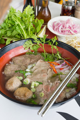 A bowl of traditional vietnamese beef and chicken pho street food, surrounded by fresh herbs. Pho is a vietnamese noodle soup consisting of meat, herbs, chilli, coriander and dumplings.