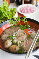 A bowl of traditional vietnamese beef and chicken pho street food, surrounded by fresh herbs. Pho is a vietnamese noodle soup consisting of meat, herbs, chilli, coriander and dumplings.