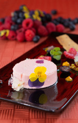 A beautiful rich gourmet blueberry and raspberry cheesecake, garnished with rose petals on a modes black plate.