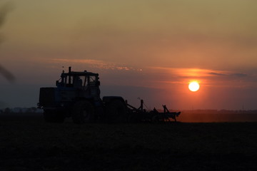 Tractor plowing plow the field on a background sunset. tractor silhouette on sunset background