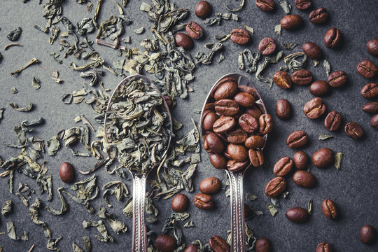 Green tea leaves and coffee seeds on metal spoons.