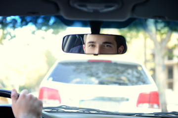 Young successful driver looking in rear view mirror