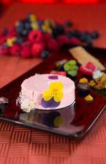 A beautiful rich gourmet blueberry and raspberry cheesecake, garnished with rose petals on a modes black plate.