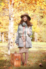Beautiful young woman with suitcase in a autumn park