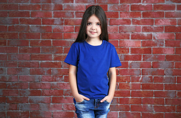 Little girl in blank blue t-shirt standing against brick wall