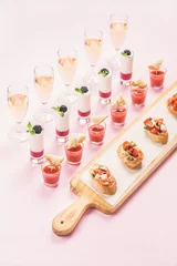 Tuinposter Catering, banquet, party food concept. Various snacks, brushetta sandwiches, gazpacho shots, desserts on corporate event, christmas, birthday, wedding celebration over pink background, selective focus © sonyakamoz