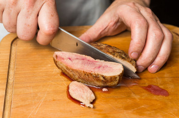 A free range, succulent pan fried duck breast fillet being sliced on a warm rustic wooden cutting board.