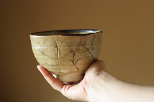 金継ぎされた茶色の抹茶茶碗を女性が右手で持つ ぼかし背景