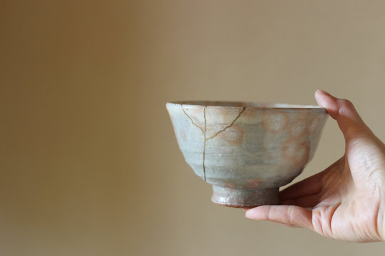 金継ぎされた日本のピンクの抹茶茶碗を片手で持つ　ぼかし背景
