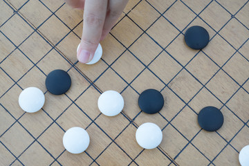 Close up view of hand playing black and white stone pieces on Chinese go game board.