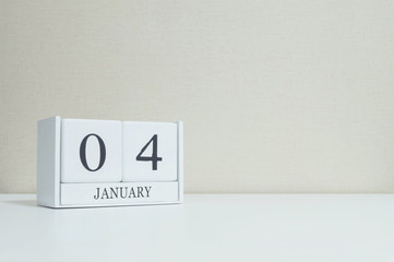 Closeup white wooden calendar with black 4 january word on blurred white wood desk and cream color wallpaper in room textured background with copy space , selective focus at the calendar