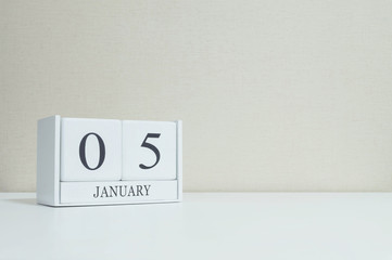 Closeup white wooden calendar with black 5 january word on blurred white wood desk and cream color wallpaper in room textured background with copy space , selective focus at the calendar