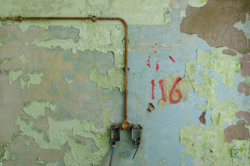 An old metal electricity cable on a green and blue textured wall, in a room with peeling paint , in an abandoned building. Exploring urban decay.